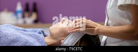 Junge Frau liegt entspannt auf Massageliege in kosmetischen Salon, eine Gesichtsbehandlung und wohltuenden Massage verwöhnen. Stockfoto