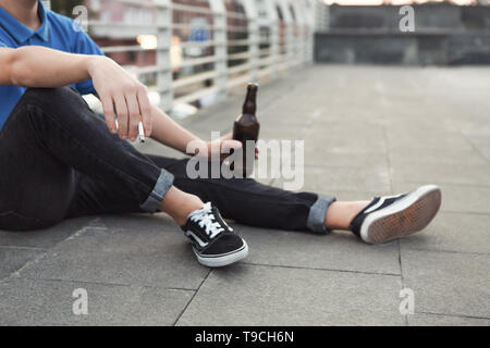 Teen guy rauchen Zigaretten und Bier trinken, sitzen nur Stockfoto