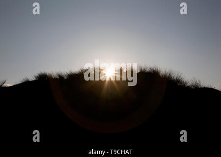 Unter der Morgen (oder Abend) Sky die sandigen Dünen silhouetted, eingesäumt durch ihre stacheligen Gras, die Sonne bricht sich hinter Ihnen. Stockfoto