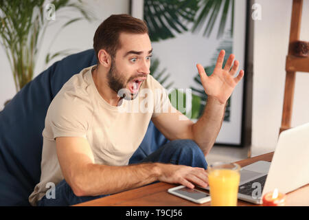 Junger Mann mit Laptop zu Hause Schockiert Stockfoto