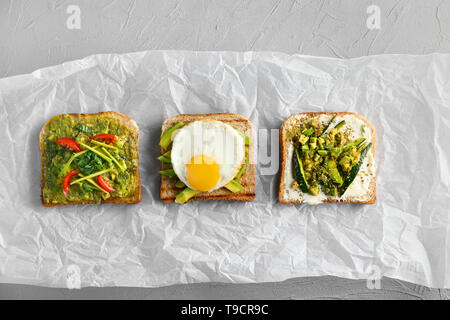Lecker geröstetes Brot mit Avocado und Spiegelei auf Pergament Stockfoto