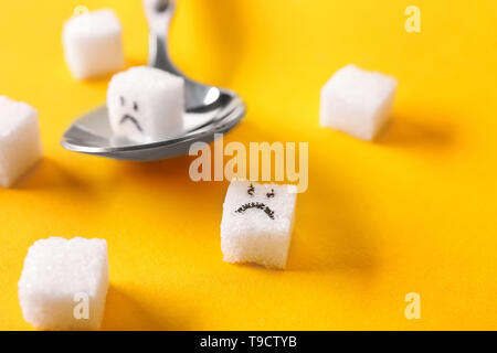 Löffel und Würfelzucker mit lustigen Gesichtern auf farbigen Hintergrund. Diabetes Konzept Stockfoto