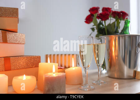 Gläser Champagner mit brennenden Kerzen und Geschenkboxen auf hölzernen Tisch Stockfoto