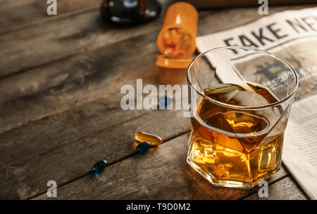 Glas Whiskey mit Pillen und Zeitung auf Holztisch. Konzept des Alkoholismus Stockfoto