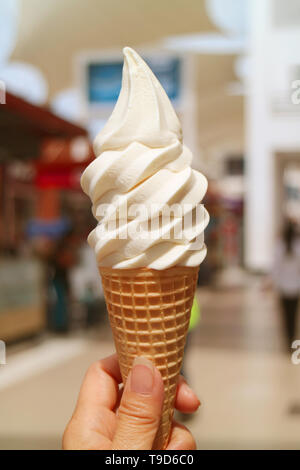 Bild vertikal von der Hand eines weiblichen Holding vanille Milch Softeis Kegel an einem sonnigen Tag Stockfoto
