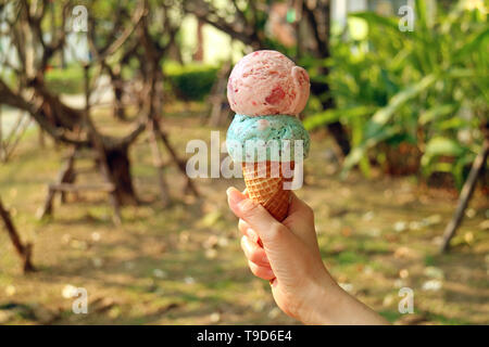 Zwei Kugeln Eis Konus in der Frau die Hand mit verschwommenen sunshine garden im Hintergrund Stockfoto