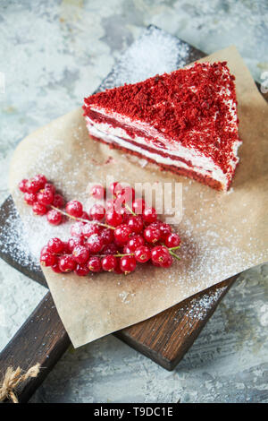 Red Velvet Cake und ein Paar rote Johannisbeeren auf einem Holzbrett. Grau strukturierten Hintergrund. Nachtisch. Lebensmittelkette Stockfoto