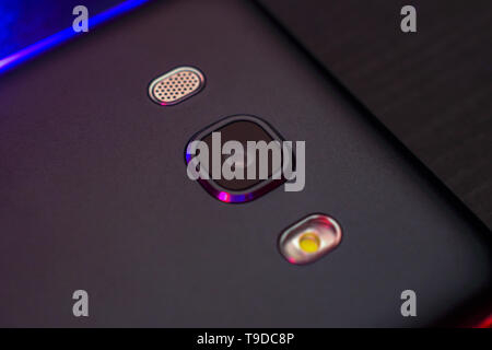Close-up des Telefons objektiv in schwarz mit dunklen blauer Hintergrundbeleuchtung, Ansicht von oben. Die Rückseite des Smartphones. Makro Foto eines horizontalen Farbe. Stockfoto