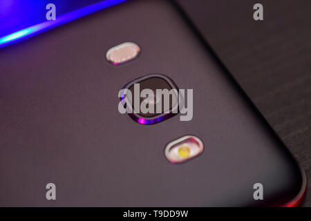 Close-up des Telefons objektiv in schwarz mit dunklen blauer Hintergrundbeleuchtung, Ansicht von oben. Die Rückseite des Smartphones. Makro Foto eines horizontalen Farbe. Stockfoto