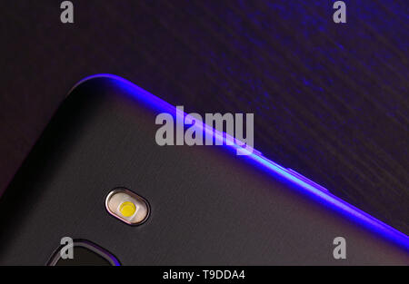 Ein Fragment der Cell Phone Case in Schwarz mit blauer Hintergrundbeleuchtung. Das Telefon liegt auf dem Schwarzen technologische Oberfläche der Kamera mit blauen Neon ligh Stockfoto