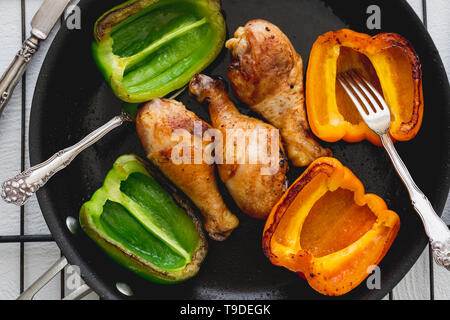 Chicken Drumsticks und gebratene grüne und gelbe Paprika in einer Pfanne Draufsicht Nahaufnahme Stockfoto