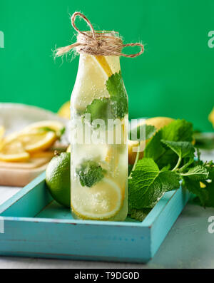 Kaltes Getränk mit Zitronen, Minze, Limette in einer Glasflasche, in der Nähe der Zutaten für Limonade, grüner Hintergrund Stockfoto