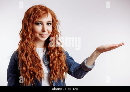 Lächelnd curly rothaarige Frau überraschen mit Ihrem Produkt isoliert auf einem weißen Hintergrund. Glückliche Frau, die mit der offenen Hand etwas halten. Adv Stockfoto