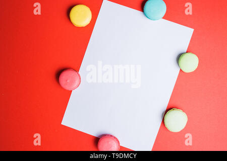 Kopieren Sie Platz für Text und Werbung. Vertikale weiße Papier auf rotem Hintergrund mit bunten Makronen. Stockfoto