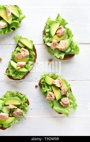 Thunfisch Sandwiches mit Avocado und Salatblätter über hellen Hintergrund. Lecker Thunfisch Brötchen zum Frühstück. Gesunden Snack. Ansicht von oben, flach Stockfoto