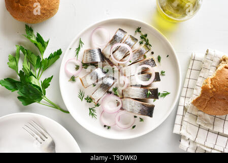 In Scheiben geschnitten gesalzene Heringe mit Gewürzen, Kräutern und Zwiebeln auf Platte am weißen Stein Hintergrund. Marinierter Fisch in Scheiben geschnitten. Essen mit gesunden ungesättigten Fettsäuren, Omega Stockfoto