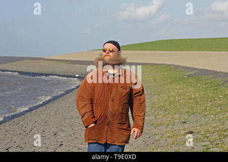 Mann mit langem Bart, der vom Wind verwirbelt wurde, steht am Ufer des Meeres Stockfoto