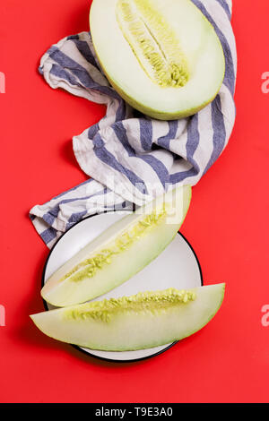 Frische Melonen geschnitten auf hellen roten Hintergrund mit gestreiften Handtuch. Ansicht von oben Stockfoto