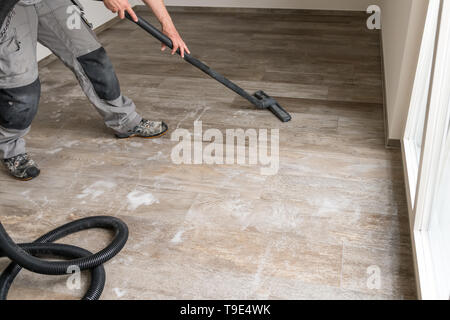 Ein Mann saugt Wasser aus dem Fliesenboden mit dem Staubsauger. Stockfoto