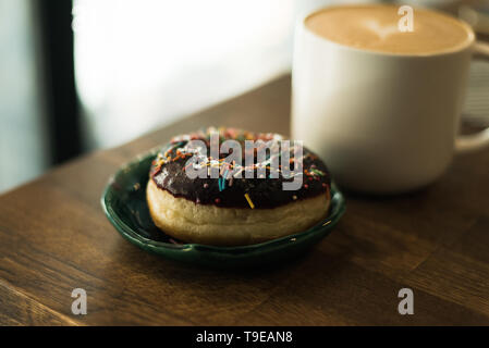 Kaffee mit einem Herz aus Milch und ein Donut auf einem Holztisch. Schlechtes Frühstück Stockfoto