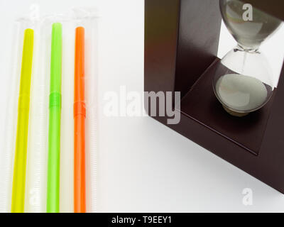Drei farbigen Plastik Strohhalme und eine Sanduhr. Weißer Hintergrund mit leeren Raum für Bildunterschrift. Plastik strohhalme sind d in verschiedenen Ländern verboten Stockfoto