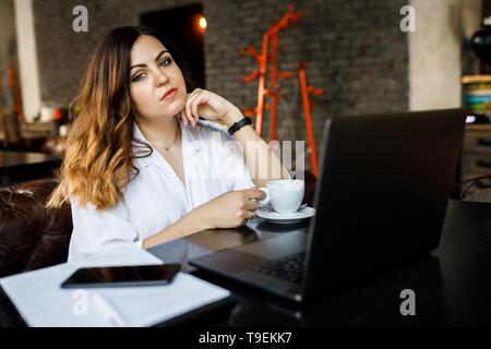 Eine junge, sympathische Frau, nicht eine dünne - vorangegangen Body Building, sitzt in einem gemütlichen Cafe, arbeiten auf einem Computer und trinkt Kaffee. Stockfoto