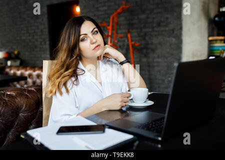 Eine junge, sympathische Frau, nicht eine dünne - vorangegangen Body Building, sitzt in einem gemütlichen Cafe, arbeiten auf einem Computer und trinkt Kaffee. Stockfoto