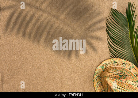 Minimalistische Sommer flach mit Palm Blätter und Panama Hut auf Sand Hintergrund mit Schatten Stockfoto