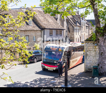 Eine Pulhams Trainer Bus an einer Haltestelle neben alten Häusern aus Stein auf dem Marktplatz in der alten Cotswold Stadt Northleach, Gloucestershire England warten Stockfoto