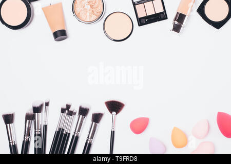 Make-up-Produkte für ebenmäßigen Teint und verschiedene Arten von Applikatoren Bürsten und Schwämme auf weißem Hintergrund, flach. Stockfoto