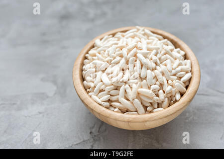 Puffreis in eine hölzerne Schüssel auf einem grauen Hintergrund, Konzept der gesunden Ernährung vegane Ernährung. Close Up, selektiver Fokus, kopieren. Stockfoto