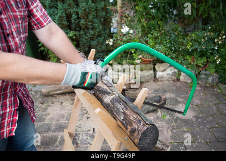 Sägen von Brennholz manuell mit einer Metallsäge auf einer hölzernen sawhorse Stockfoto