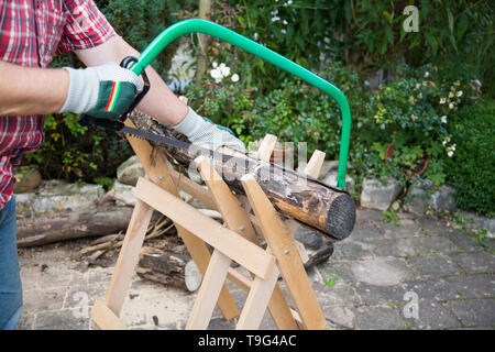 Sägen von Brennholz manuell mit einer Metallsäge auf einer hölzernen sawhorse Stockfoto