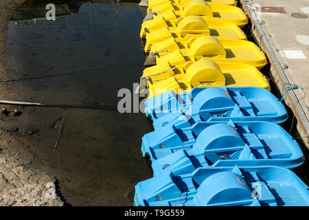 Mehrere leere bunte Tretboote stehen auf dem Wasser von der Pier am Flußufer. Unterhaltung für die Touristen. Stockfoto