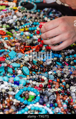 Eine Frau, deren Fingernägel lackiert Orange ist ein Armband aus roten Perlen, dass sie aus einem Stapel von bunten Halsketten und Armbänder gezogen. Stockfoto