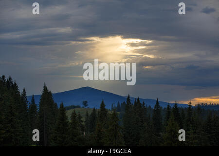 Sonne scheint durch die Lücke bei bedecktem dramatische Himmel über den Bergen. Stockfoto