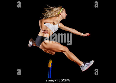 Muskulöse Sportlerin über Hürde auf Sprint Rennen auf schwarzem Hintergrund isoliert springen. Leichtathletik event Konzept Bild Stockfoto