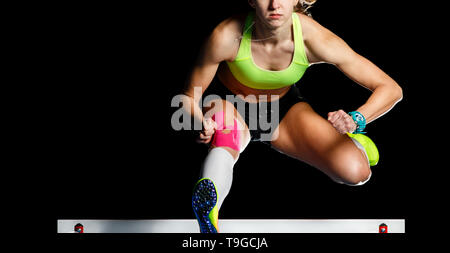 Junge Athletin über Hürde im Sprint springen. Sprinter über Hindernis auf schwarzem Hintergrund isoliert springen Stockfoto