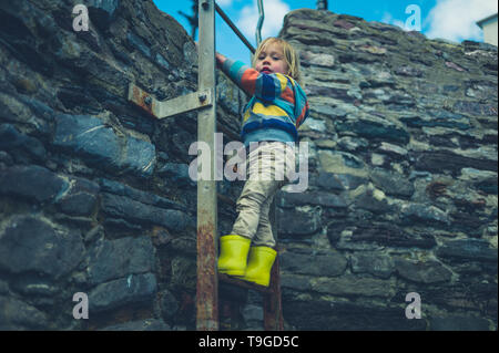 Ein kleines Kind ist Klettern eine alte Leiter auf eine Mauer aus Stein Stockfoto