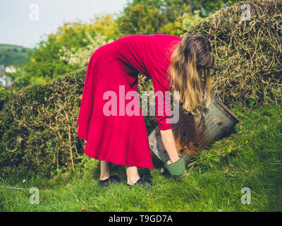 Eine junge Frau in einem eleganten Kleid ist Unkraut ziehen und Sie in eine Verbrennungsanlage Stockfoto