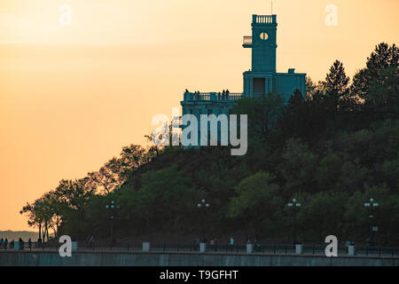 Sonnenuntergang am Ufer des Amur in Chabarowsk. Die Sonne über dem Horizont. Der Damm ist Licht der Laternen. Stockfoto