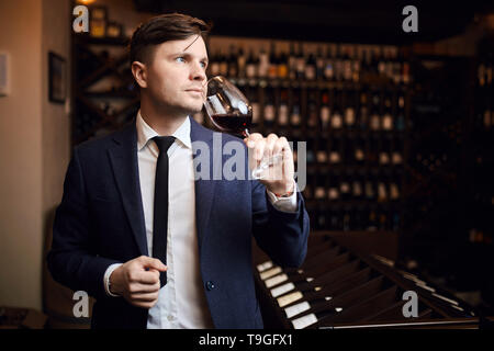 Mann hält ein Glas Wein. Verkostung und Verkostung Konzept. Schön wunderschöne Geschäftsmann im eleganten Anzug mit Glas Whiskey. Bis schließen Foto. Kopieren Sie Platz Stockfoto