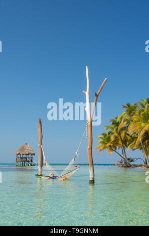 Reifer Mann entspannt in der Hängematte in tropischen Gewässern und Palapa Plattformen,Lange Coco Plum Caye, Belize Stockfoto
