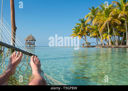 Füße und Hängematte in tropischen Gewässern und Palapa Plattformen,Lange Coco Plum Caye, Belize Stockfoto