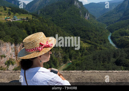 Eine junge Frau in einem weißen Bluse und Strohhut Uhren der mountain river unter den Stein Schlucht fliesst. Stockfoto