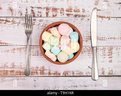 Marshmallows in einer runden Schüssel auf weißem Holz- Hintergrund. Gabel, Messer und Schüssel weiß, Holz- Hintergrund. Ansicht von oben. Stockfoto
