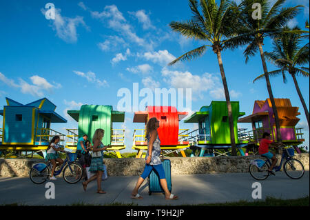 MIAMI - Juli 2017: Leute führen entlang der Miami Beach Promenade vor der Leuchtendbunten neu errichtete Rettungstürme in South Beach. Stockfoto