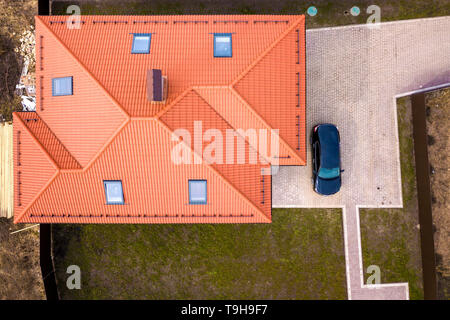 Antenne oben Ansicht des Hauses metall Schindeldach mit Dachfenster und schwarze Auto auf gepflasterten Hof. Stockfoto