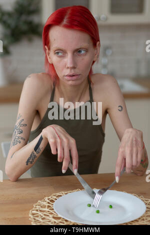 Skinny Frau mit Messer und Gabel sitzt in der Nähe der leeren Teller Stockfoto