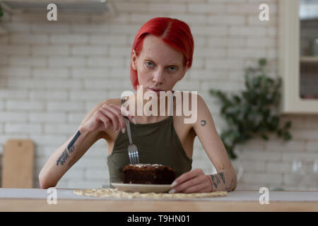 Magersüchtige Frau mit Tattoos am Tisch sitzen mit Schokolade Kuchen Stockfoto